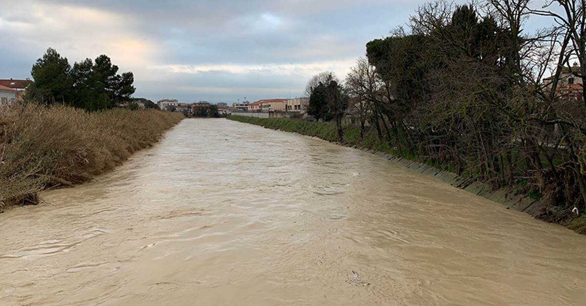 Foto scattata da un ponte in cui si vede il fiume gonfio di acqua marrone
