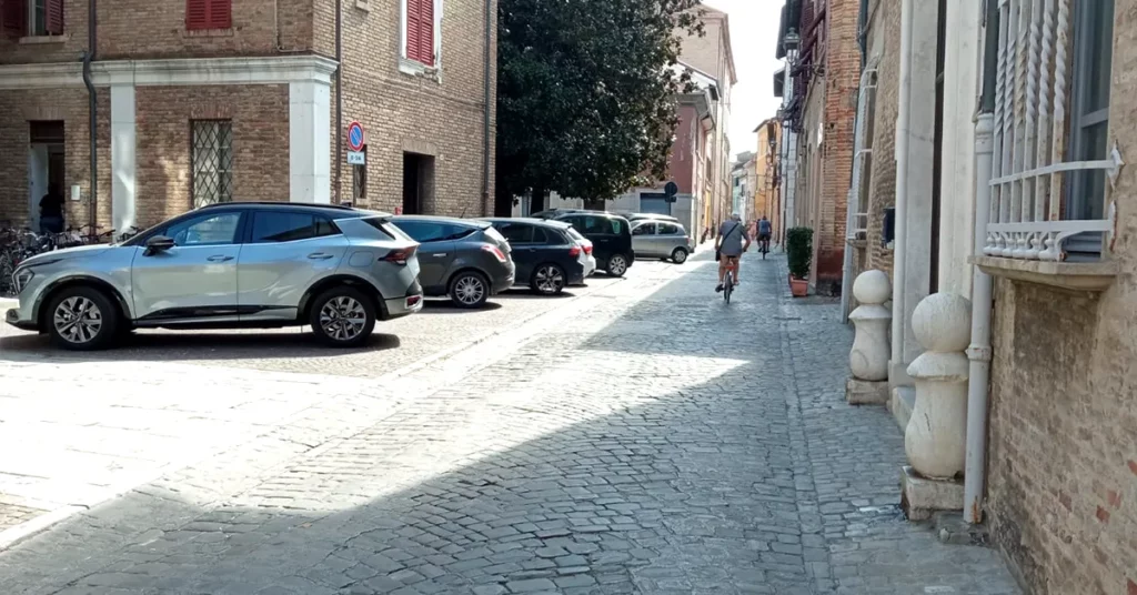 8 auto pacheggiate in via Mastai, dietro il Comune. Bici passano lungo la strada