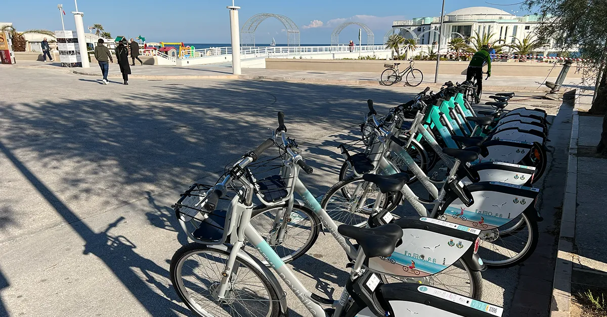 Sei biciclette color turchese, parcheggiate in batteria davanti alla rotonda.