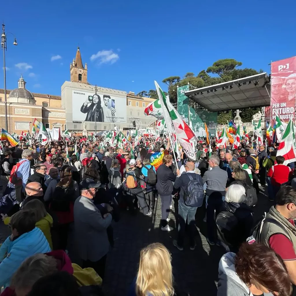 Davanti al palco è pieno di persone con le bandiere del PD