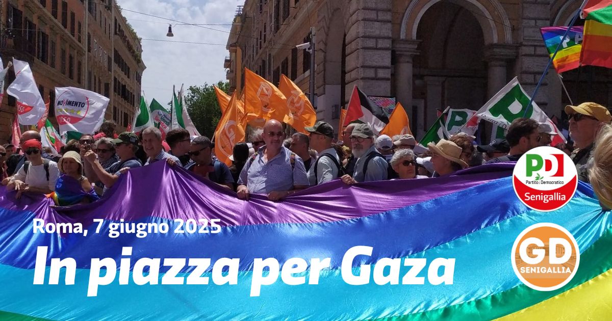 Il bandierone arcobaleno della Scuoal di Pace tenuto dalla folla. Sullo sfondo, bandiere della Pace, del PD, dei GD, del Movimento 5 Stelle, della Palestina